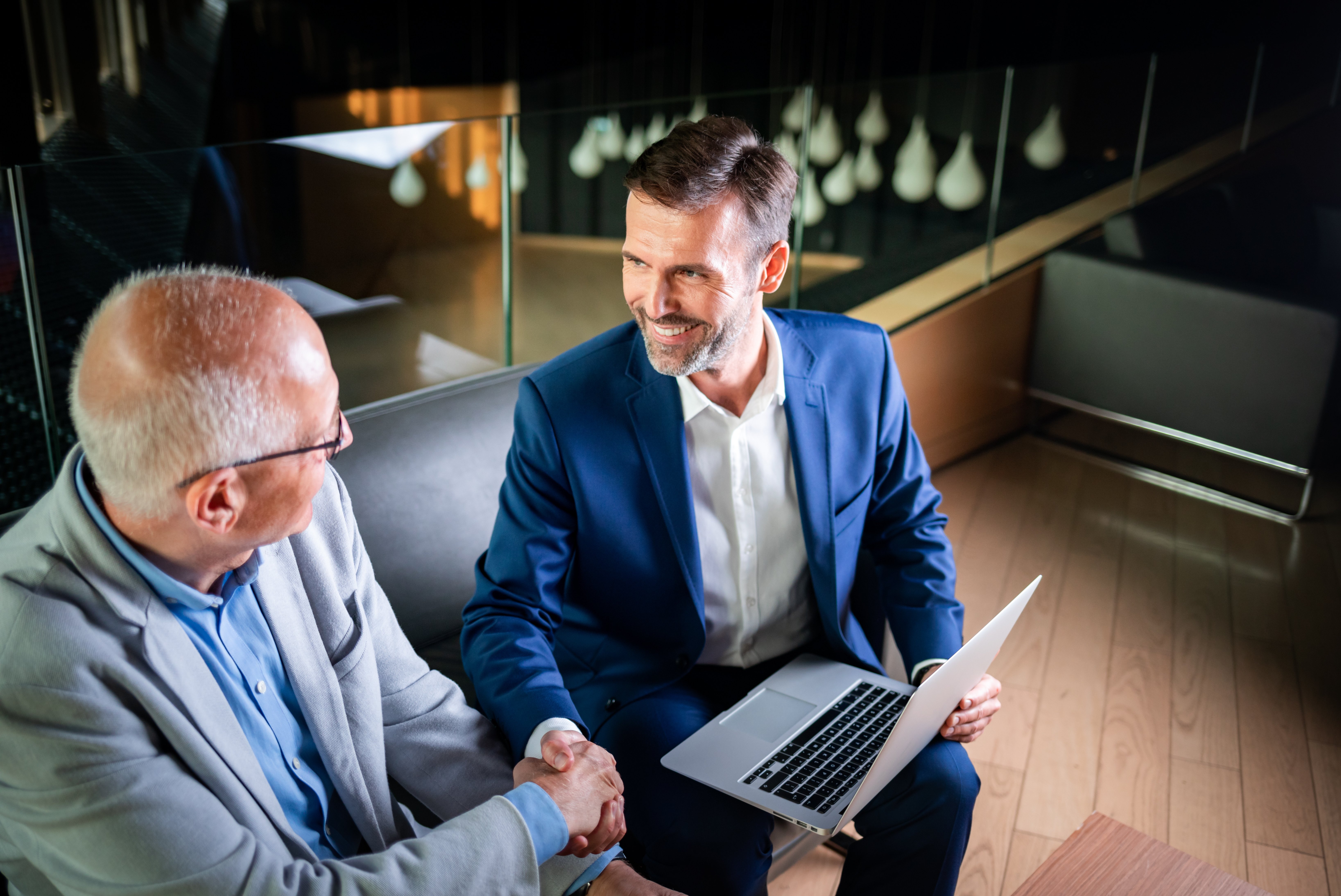 younger-and-older-businessman-shaking-hands-in-mod-2024-10-30-22-07-27-utc